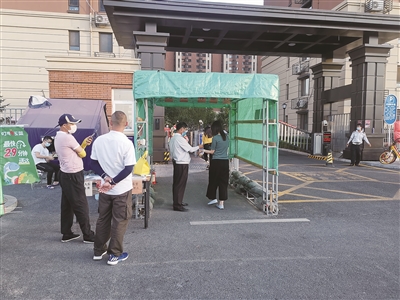 6月15日，在北京市丰台区花乡某小区门口，社区工作人员正按照要求检查居民出入证，并测量体温。  本报记者 喻大伟 摄