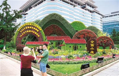 2021年6月，庆祝中国共产党成立100周年主题花坛亮相长安街沿线，西单东南角的全面小康主题花坛吸引市民驻足留影。 （图片来源：人民视觉）